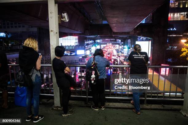 Pedestrians look out at passing traffic from a foot bridge at dusk in Bangkok, Thailand, on Wednesday, June 21, 2017. Stocks of consumer...