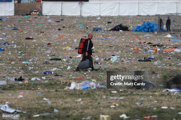 Man walks through a field covered in litter as he leaves the Glastonbury Festival site at Worthy Farm in Pilton on June 26, 2017 near Glastonbury,...