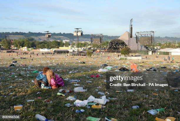 Couple sit amongst rubbish by the Pyramid Stage following the Glastonbury Festival at Worthy Farm in Pilton, Somerset.