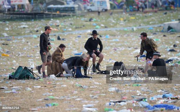 Festival goers sit amongst rubbish following the Glastonbury Festival at Worthy Farm in Pilton, Somerset.