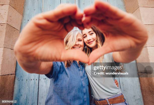 smiling senior mother and daughter making a heart shape with their hands - mother's day stock pictures, royalty-free photos & images