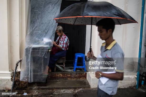 Typist works behind a tarpaulin in the doorway of a building as a pedestrian holding an umbrella passes by in Yangon, Myanmar, on Wednesday, June 14,...