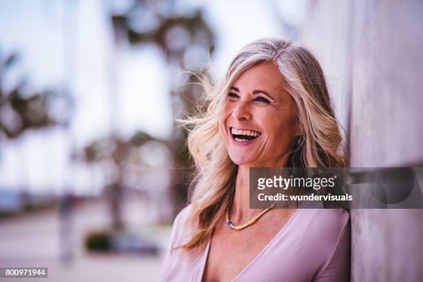 beautiful stylish senior woman laughing leaning against wall outdoors - wavy hair stock pictures, royalty-free photos & images