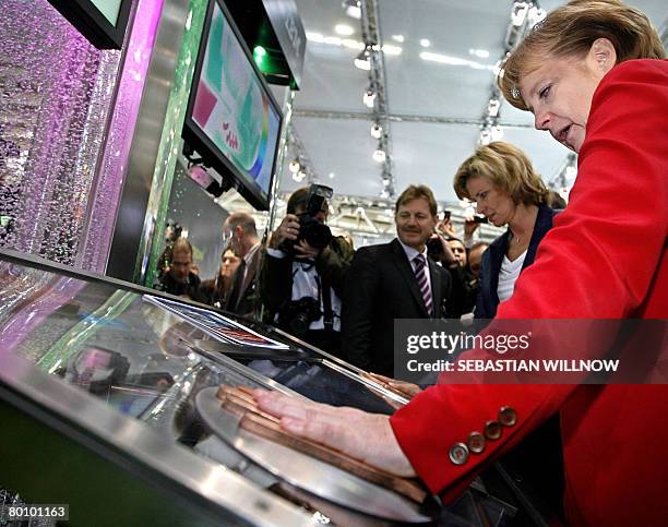 German Chancellor Angela Merkel puts her hand on a scanner measuring her temperature as she visits the stand of IBM during her opening visit of the...