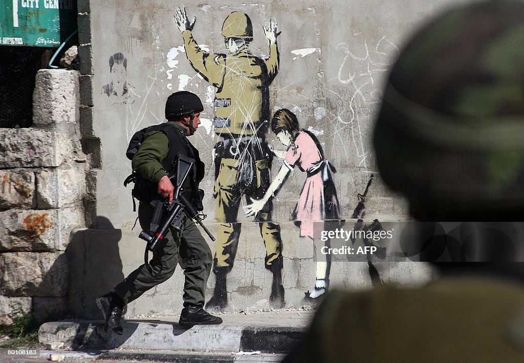 An Israeli soldier runs past a wall mura