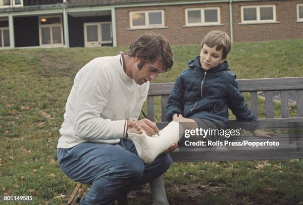 English professional footballer and forward with West Ham United Football Club, Geoff Hurst signs the plaster cast on the leg of a young boy fan...