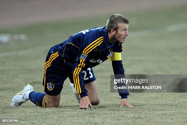 English football star David Beckham from the LA Galaxy team, crouches on the ground after being tackled during their exhibition match against a joint...