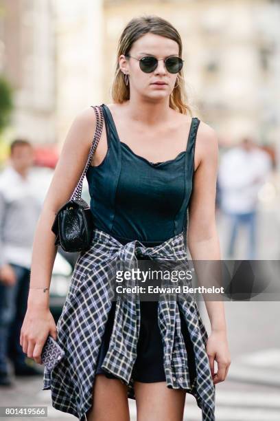 Guest wears sunglasses, a black off shoulder sleeveless top, a gigham vichy shirt, and a black bag, outside the Kenzo show, during Paris Fashion Week...