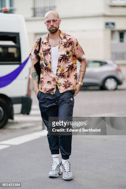 Guest wears sunglasses, a white t-shirt, and opened flower print shirt, black pants, gray shoes, outside the Kenzo show, during Paris Fashion Week -...