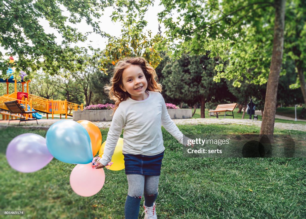 Happy kid girl playing with colorful bunch of balloons