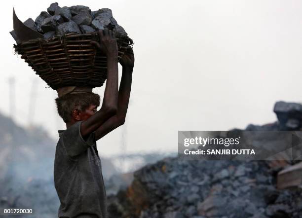 An Indian coal scavenger carries a basket of coal collected at a mine in the district of Dhanbad in the state of Jharkhand on June 27, 2017. - Coal...