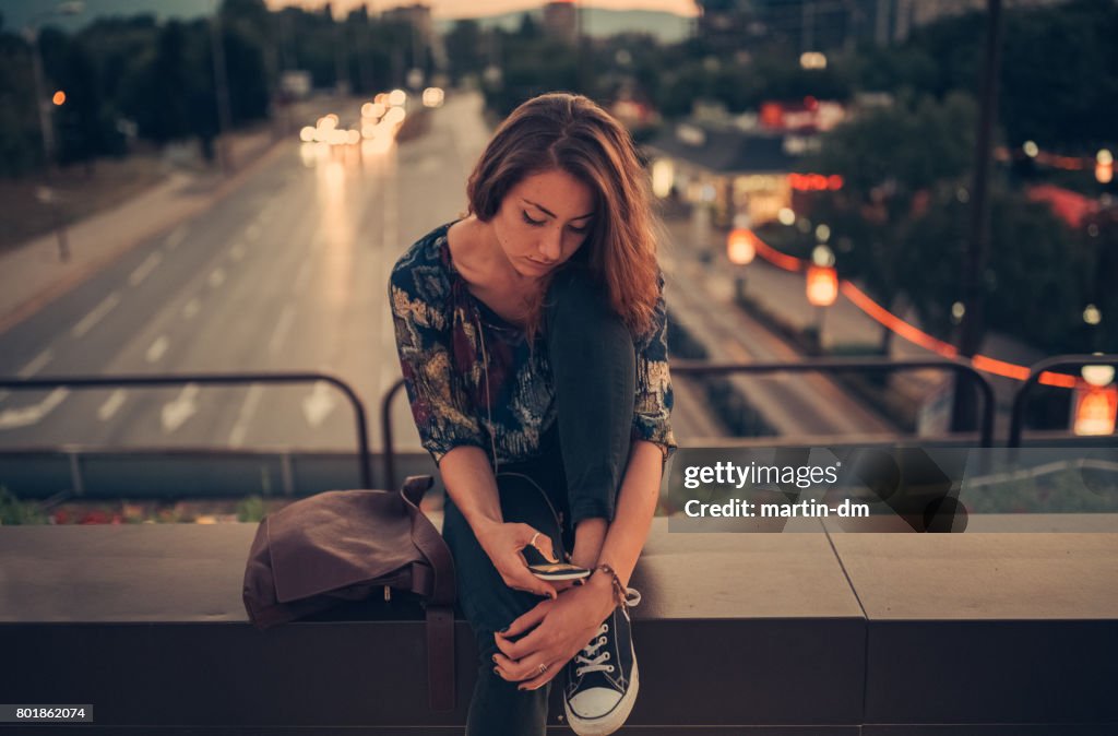 Depressed teenage girl texting on the bridge