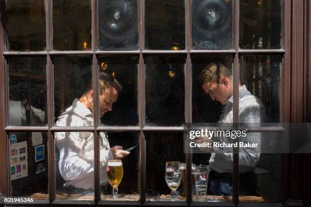 Two businessmen look at their phones in the window of a pub in Lime Street in the heart of the capital's financial district, on 26th June, in the...