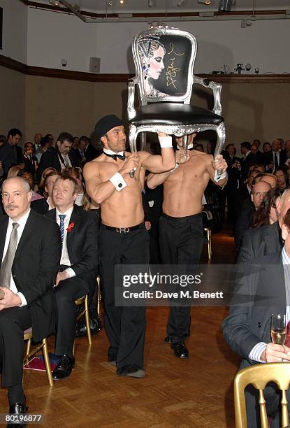 Men bring out an autographed 'Kylie' chair by Jimme Martin at the The Lighthouse Gala Auction in aid of the Terrence Higgins Trust held at Christie's...