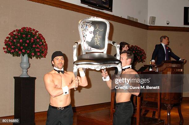 Men bring out an autographed 'Kylie' chair by Jimme Martin at the The Lighthouse Gala Auction in aid of the Terrence Higgins Trust held at Christie's...