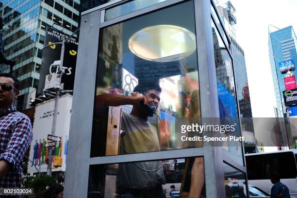 Jerome Farah and Kelly Missal stand in a repurposed telephone booth in Times Square as part of artist Aman Mojadidi's interactive public art...