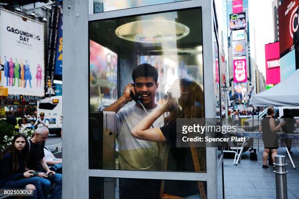 Jerome Farah and Kelly Missal stand in repurposed telephone booths in Times Square as part of artist Aman Mojadidi interactive public art...