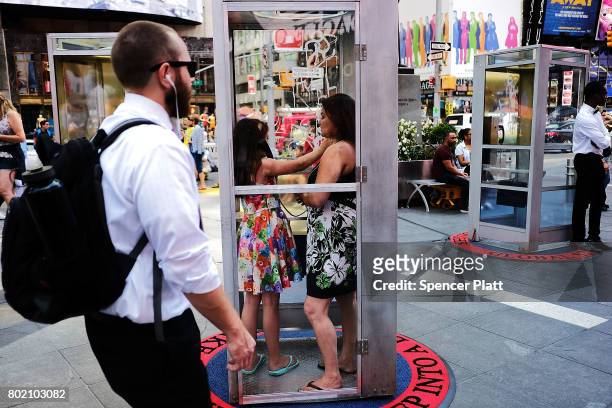 People stand in a repurposed telephone booth in Times Square and listen to the receiver as part of artist Aman Mojadidi interactive public art...