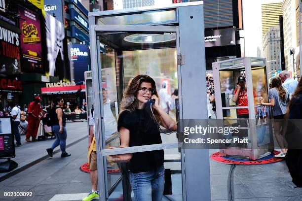 Kelly Missal stands in a repurposed telephone booth in Times Square and listens to the receiver as part of artist Aman Mojadidi interactive public...