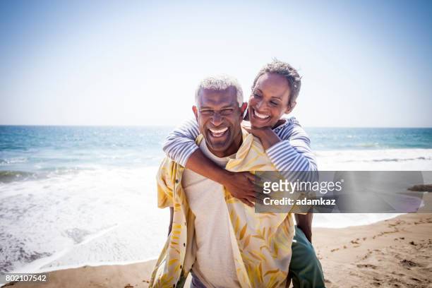 piggyback di coppia nera sulla spiaggia - coppia anziana foto e immagini stock