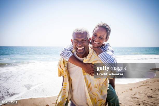 black couple piggyback on beach - active seniors beach stock pictures, royalty-free photos & images