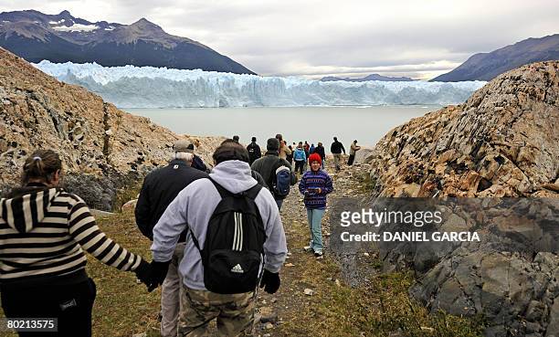 Tourists walk toward the Perito Moreno glacier base through a rocks field, a sand beach and a lenga's forest to do the mini-trekking February 28,...