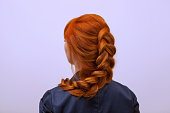 Beautiful girl with long red hair, braided with a French braid, in a beauty salon.