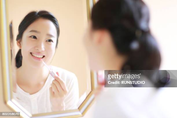 young woman applying make-up in mirror - lipgloss stockfoto's en -beelden