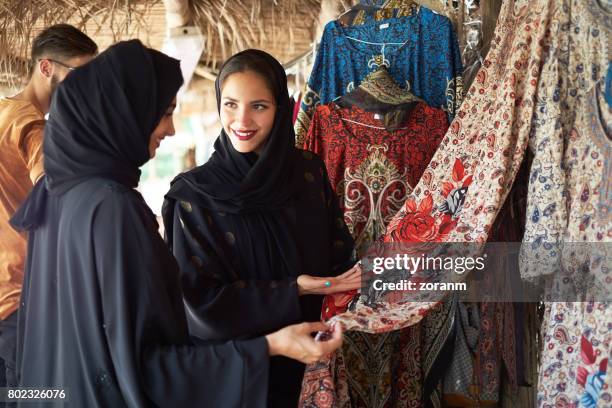 middle eastern women checking out displayed dress - abaya clothing stock pictures, royalty-free photos & images