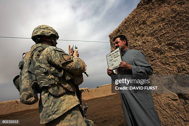 Soldier from Ghostrider Company 3rd Squadron 2nd Stryker Cavalry Regiment photographs an Iraqi villager holding a placard with his personal data...