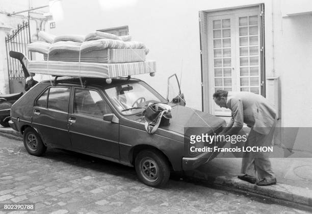 Un homme attache un lit et des matelas sur le toit de sa voiture lors d'un départ en vacances en juillet 1988 à Paris, France.