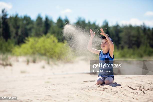 little boy throwing sand on the beach - skandinavischer abstammung stock-fotos und bilder