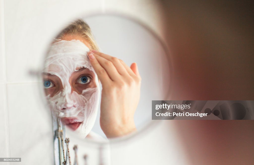 A Young woman with blue eyes applying a beauty mask.