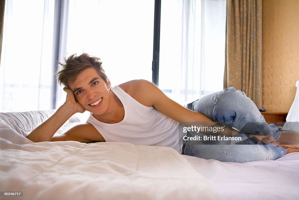 Young man smiles lays on bed.