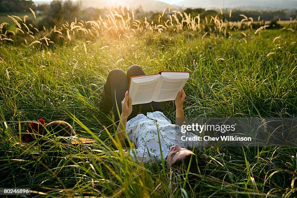 woman lying in grass reading. - romance book stock pictures, royalty-free photos & images