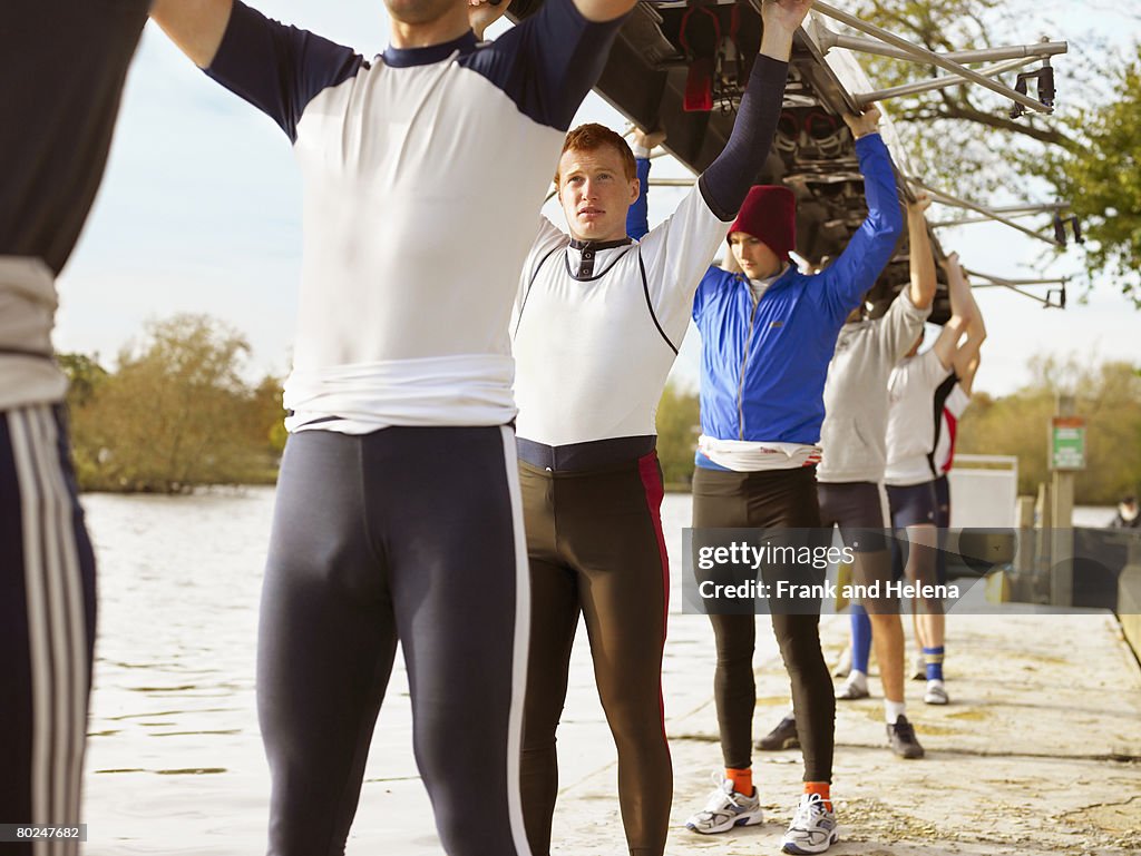 Crew with boat above heads on river bank.