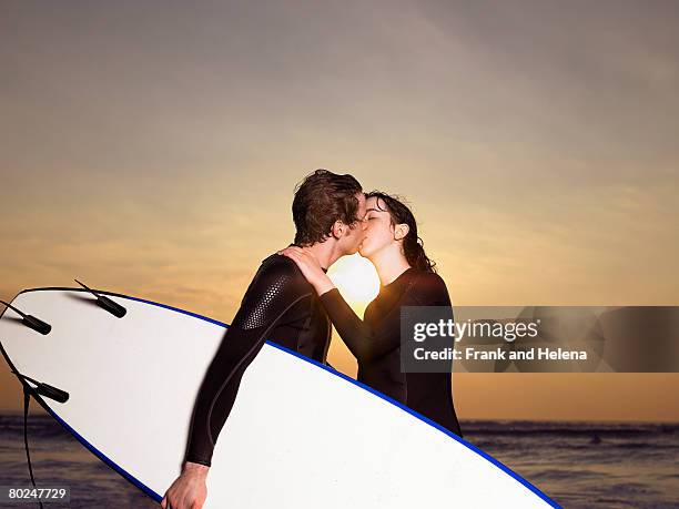 surfer couple kissing on a beach. - croyde beach stock pictures, royalty-free photos & images