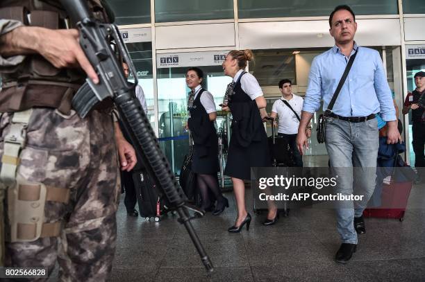 An armed Turkish special forces police officer stands guard near a gate as stewardesses walk past during a memorial ceremony on June 28, 2017 at...