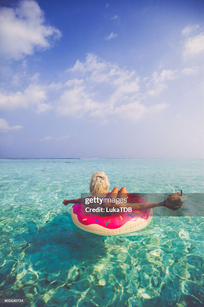 Blonde woman chilling and floating on inflatable doughnut in ocean, Maldives