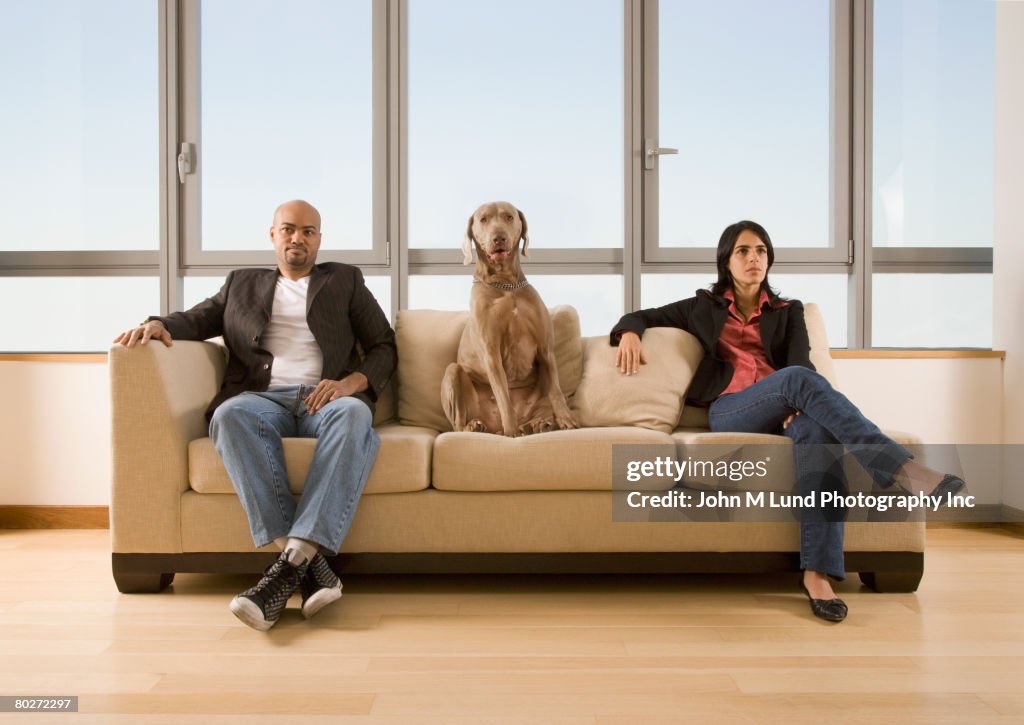 Multi-ethnic couple and dog sitting on sofa