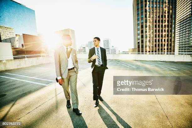 two businessmen in discussion while walking on downtown parking garage rooftop - buildings side by side stock pictures, royalty-free photos & images