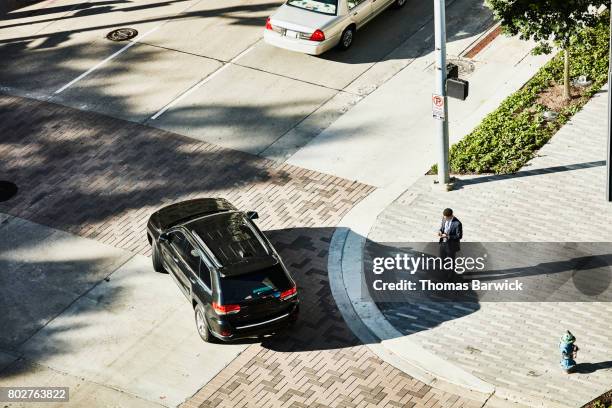 overhead view of businessman on downtown street corner checking smartphone - vehículo terrestre fotografías e imágenes de stock