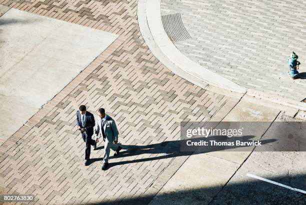 overhead view of two businessmen in discussion walking across downtown street - businessman high angle stock pictures, royalty-free photos & images