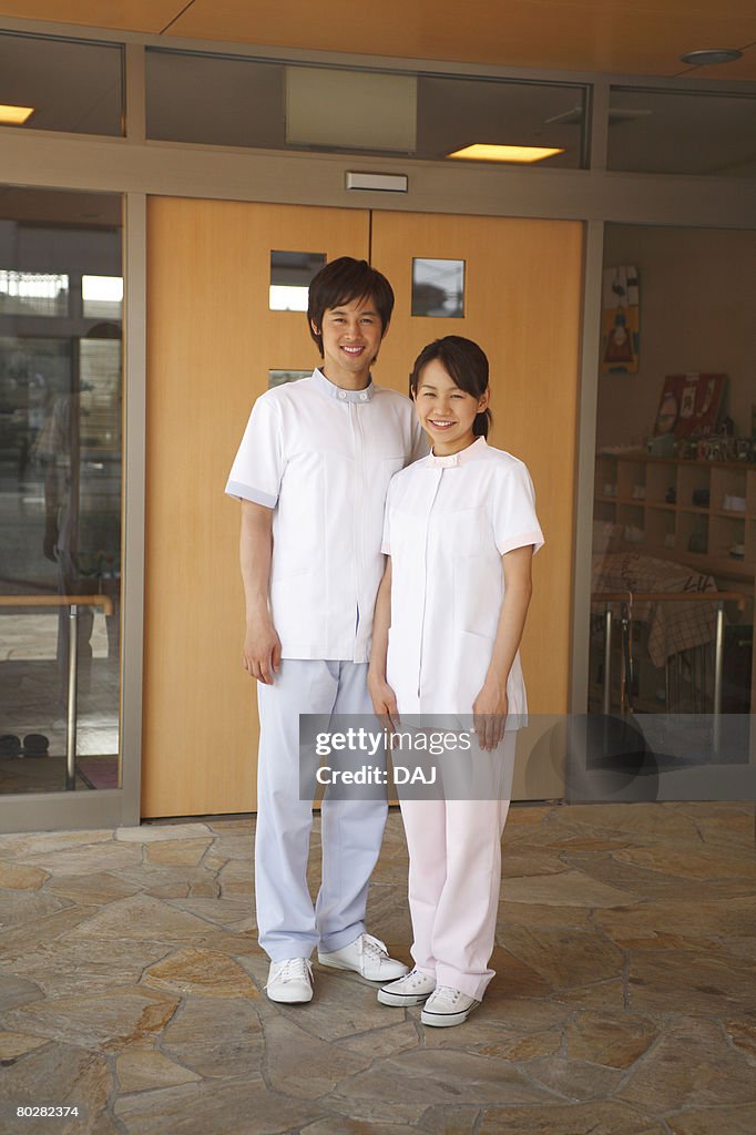 A Young Woman and A Young Man Smiling, Serving Elderly Care, Looking at Camera