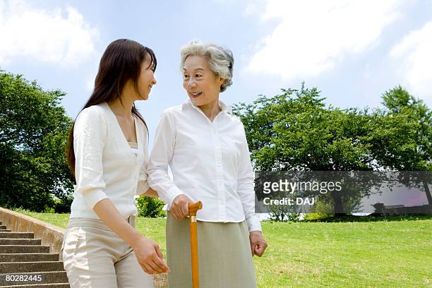 woman helping senior woman walking down stairs, smiling - grandma cane stock pictures, royalty-free photos & images
