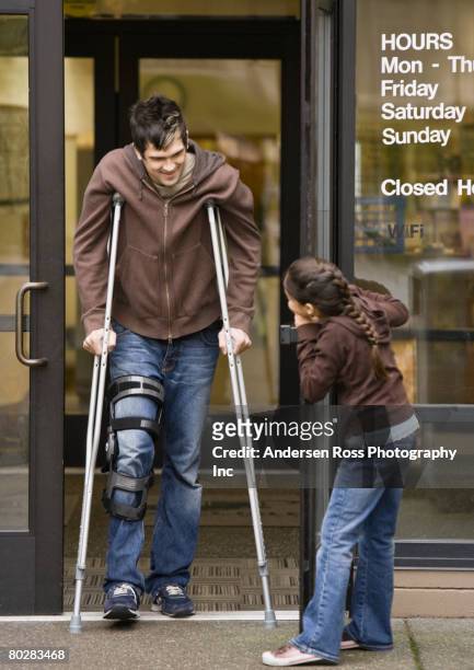 mixed race girl holding door for man on crutches - kindness stock-fotos und bilder