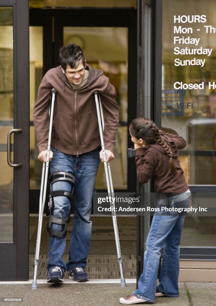 Mixed Race girl holding door for man on crutches