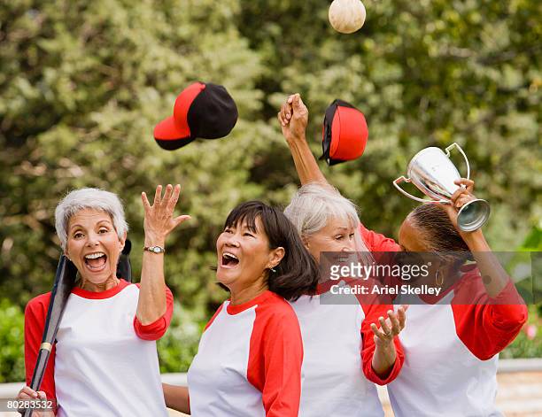 multi-ethnic senior women in baseball uniforms cheering - softball sport stock-fotos und bilder