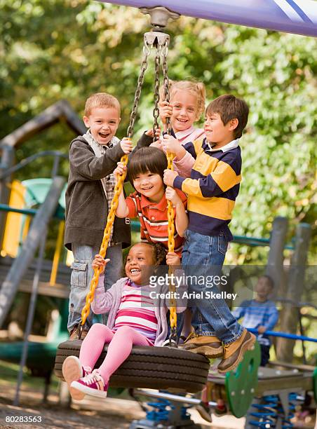 multi-ethnic children playing on tire swing - área de juego fotografías e imágenes de stock
