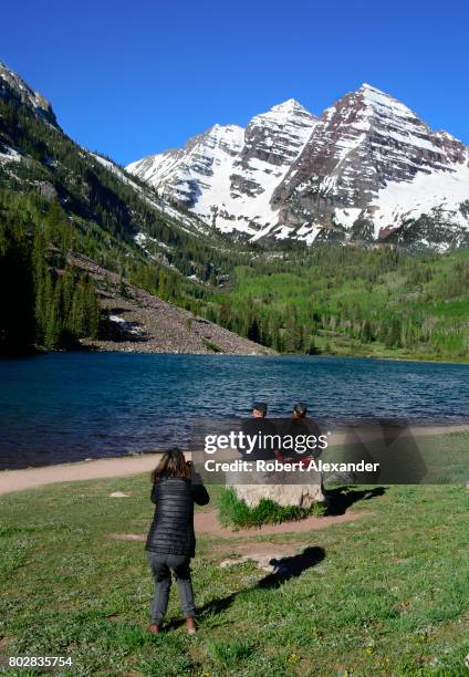 Photographer takes a picture of a couple admiring Maroon Lake and the Maroon Bells in the background. The Maroon Bells, near Aspen, Colorado, are two...